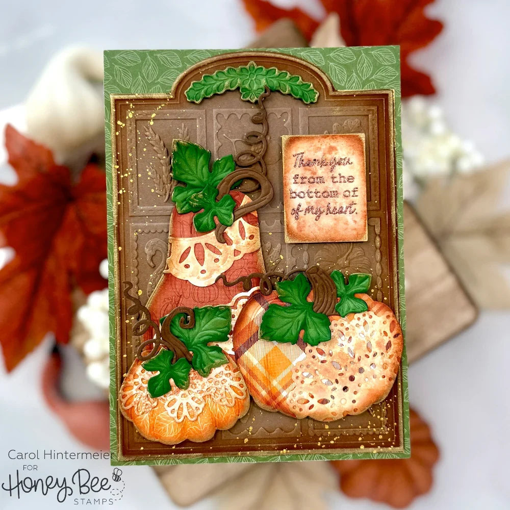 A handmade autumn-themed greeting card featuring three decorated pumpkins, green leaves, and a small message card that reads, 'Thank you from the bottom of my heart.' The card is displayed against a soft, blurred background of fall leaves and pumpkins.