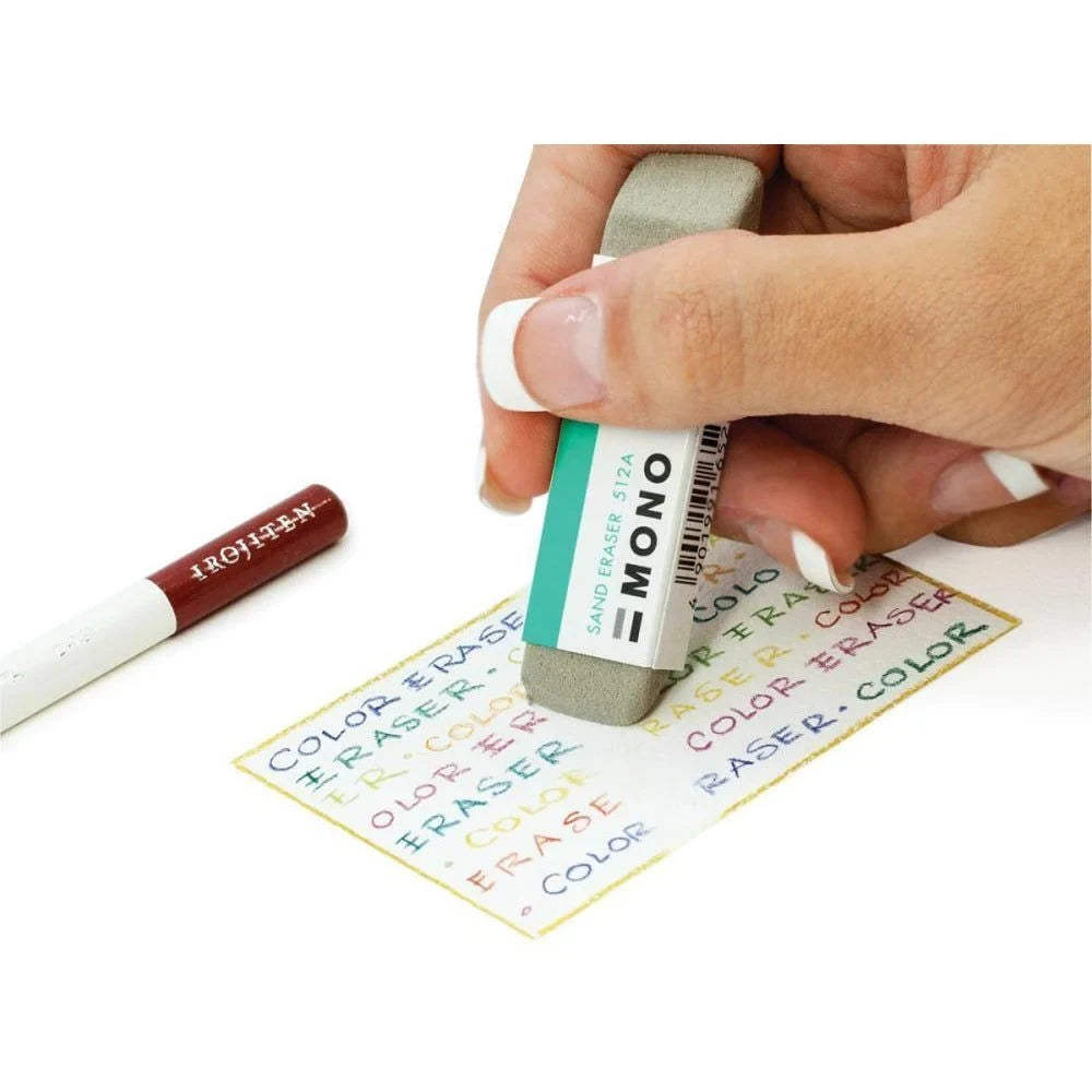 A hand using a Tombow Mono Zero Sand Eraser to remove colored ink from paper.