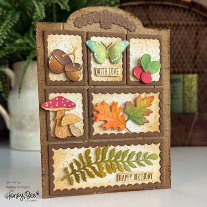 A handmade autumn-themed greeting card with a rustic brown wood-grain frame and six decorative panels featuring acorns, a butterfly, berries, a mushroom, fall leaves, and a fern. The bottom panel reads 'HAPPY BIRTHDAY'.
