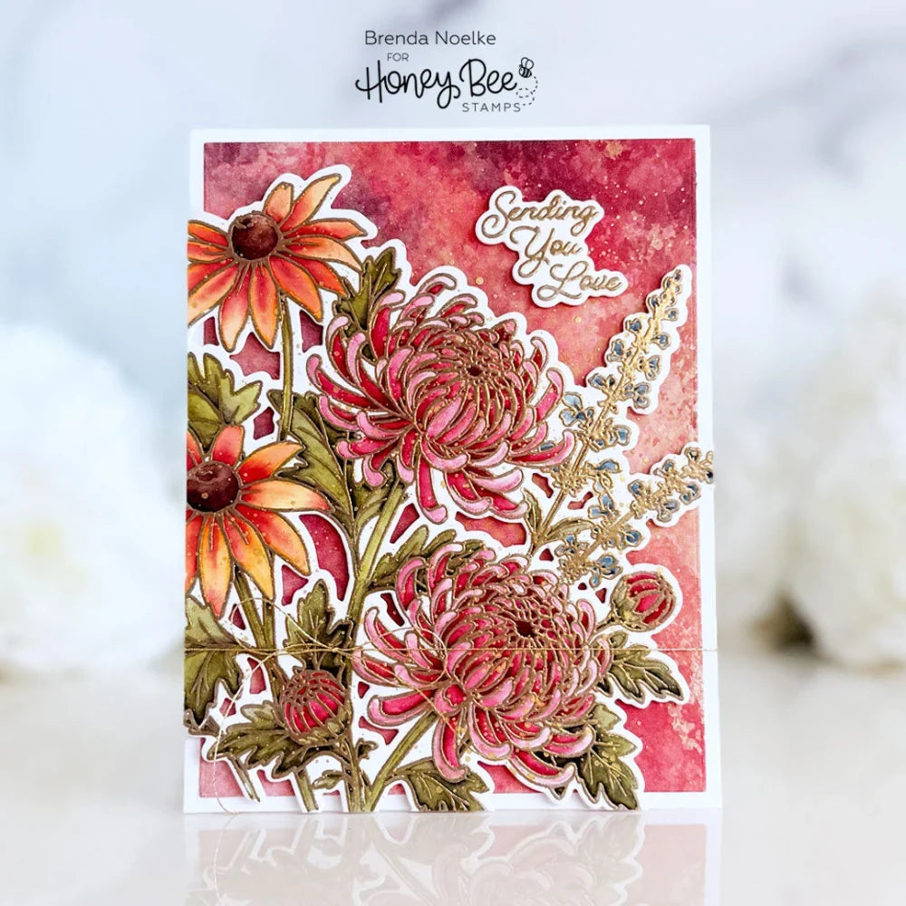 A handmade layered card featuring three dimensional floral cutouts in shades of pink, orange, and green over a textured red and pink watercolor background. The card has a white border and a die-cut script reading 'Sending You Love'.