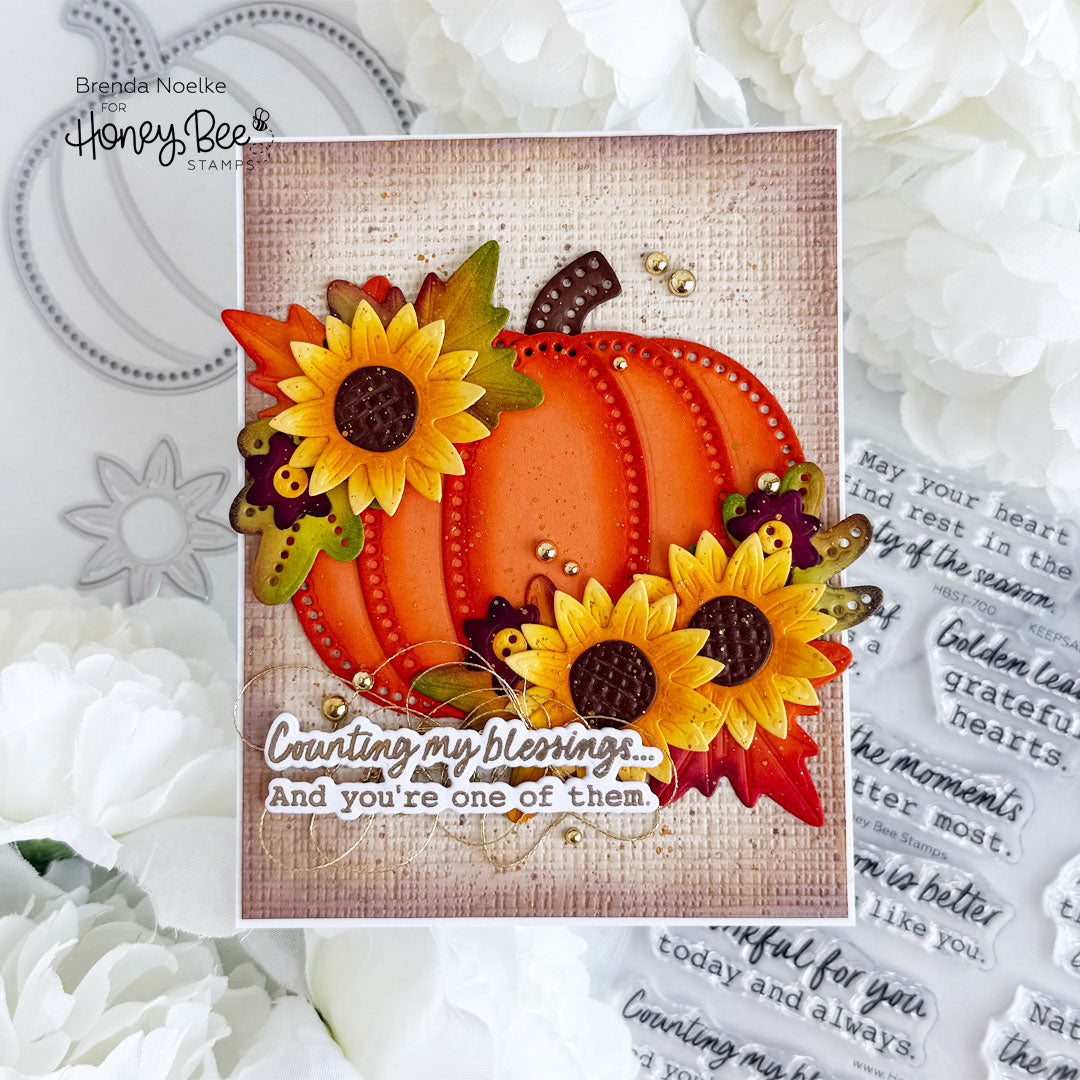 A handmade autumn-themed greeting card featuring a layered orange pumpkin, yellow sunflowers, and fall leaves on a burlap-textured background, with the phrase 'Counting my blessings.