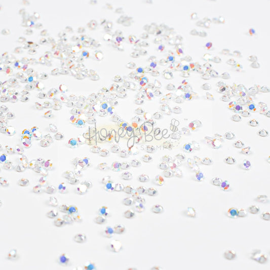 Scattered 2.3mm Crystal AB faceted rhinestones by Honey Bee Stamps on a white background.