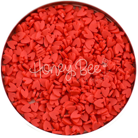A circular container filled with small, red clay heart embellishments by Honey Bee Stamps.